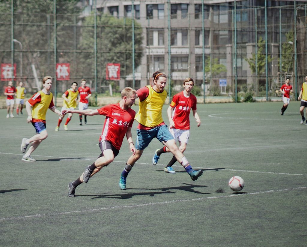 Männer spielen Fußball auf einem Fußballplatz mit Zaun.